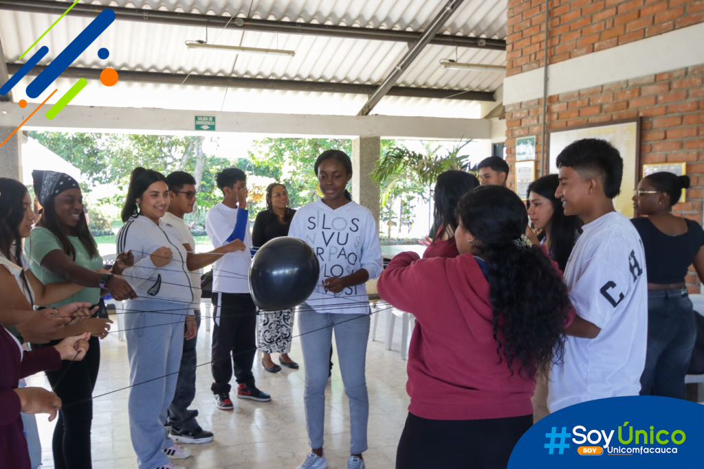 Estudiantes de la jornada diurna realizando un actividad en equipo de pasar un globo negro sostenido por hilos de lana.