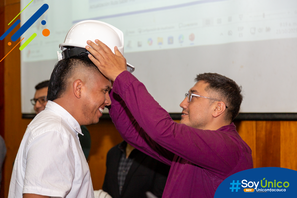 Estudiante de décimo semestre recibiendo su casco por parte de uno de nuestros docentes de Ingeniería Industrial.