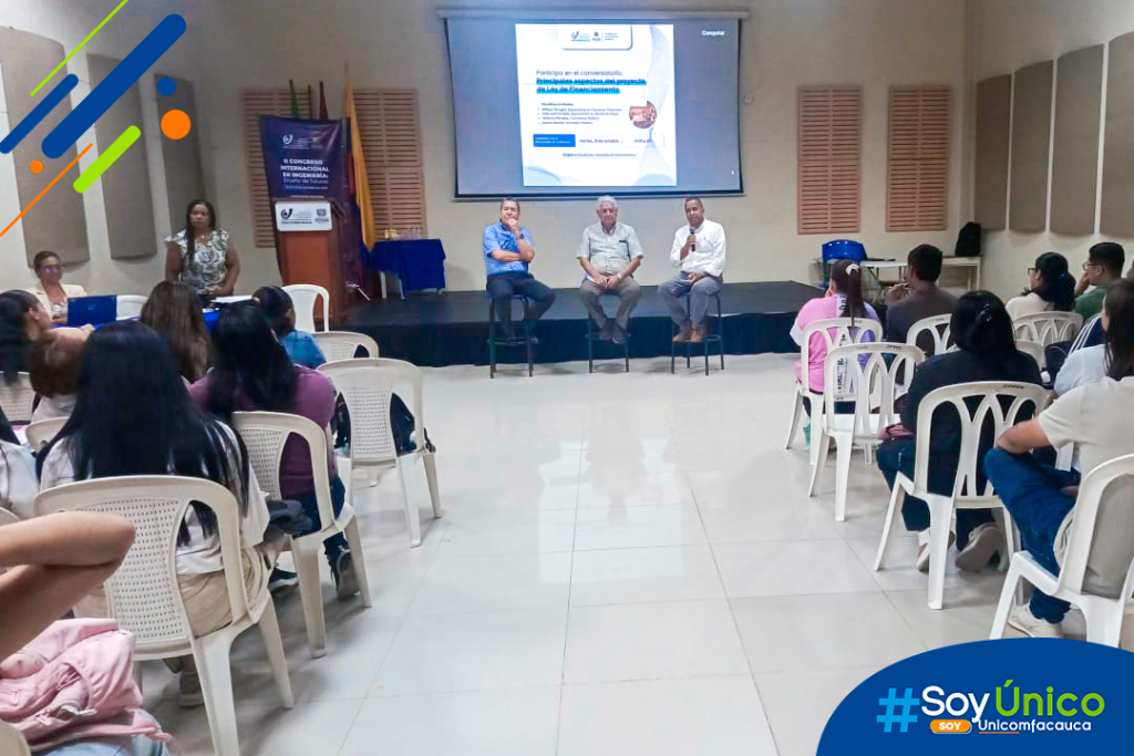 Fotografía general de espaldas donde se ven los asistentes, invitados y mesa principal del Conversatorio.