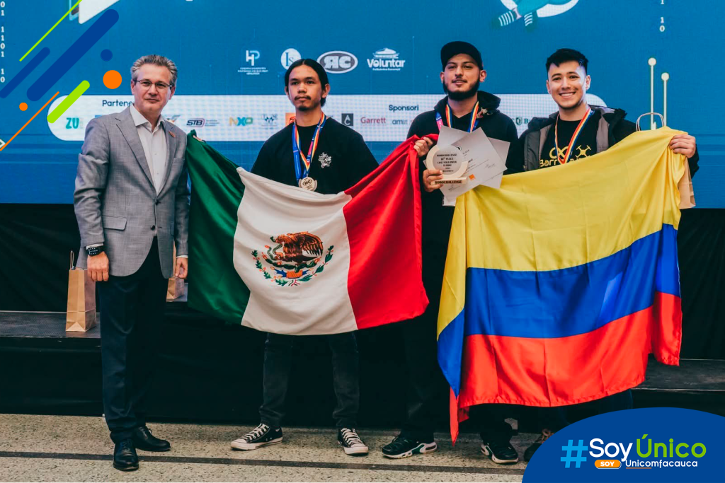 Juan Carlos Barrera y Felipe Burbano sosteniendo la bandera de Colombia al lado del ganador del primer lugar sosteniendo la bandera de méxico.
