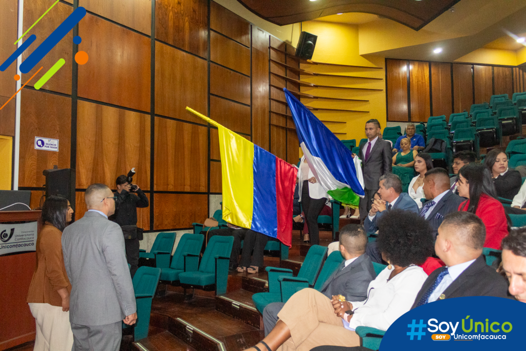 Laura Valentina Pajoy Hurtado y José Manuel Pizo Cometa, haciendo la entrega de la bandera institucional a  Johanna Acosta Enriquez y Juan Pablo Ortiz Parra.