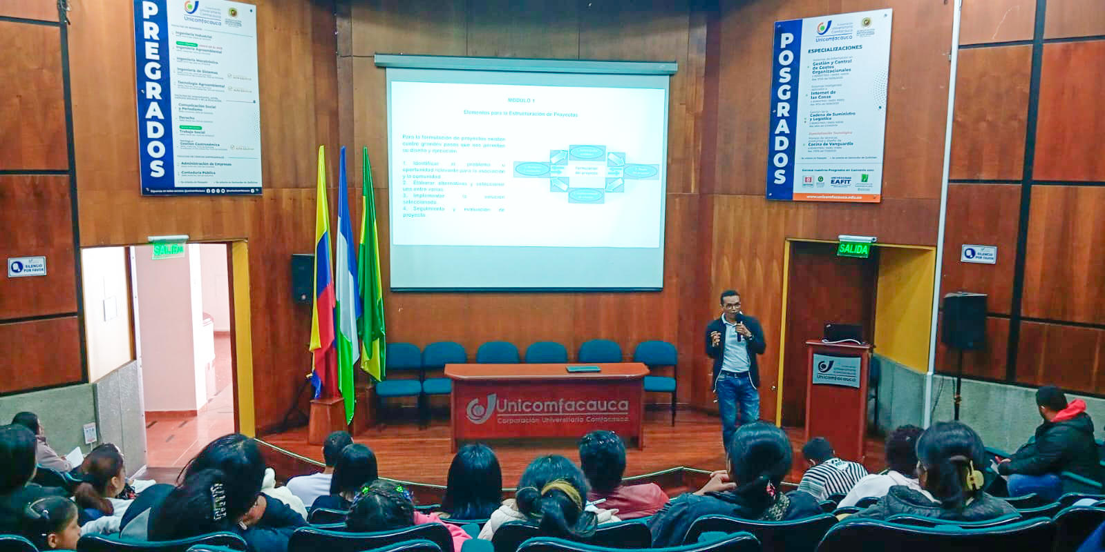 Fotografía de espaldas general del Auditorio Julio Arboleda, en donde los asistentes están mirando hacia el frente atendiendo la información que da un docente.