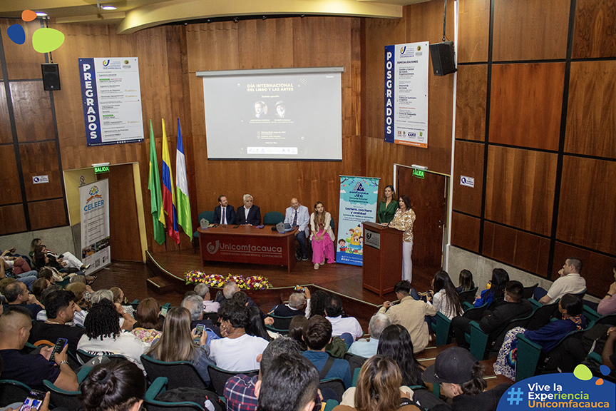 Fotografía en plano general en donde se puede visualizar el publico de espaldas y la mesa principal enfocada. En la mesa principal se encuentra Juan Esteban Constaín, el Dr. Juan Cristobal Velasco Cajiao, Humberto Dorado, Adriana Vidal, Paola Martinez y la Dra. Lina Uribe Correa en el atril dando su discurso de apertura.